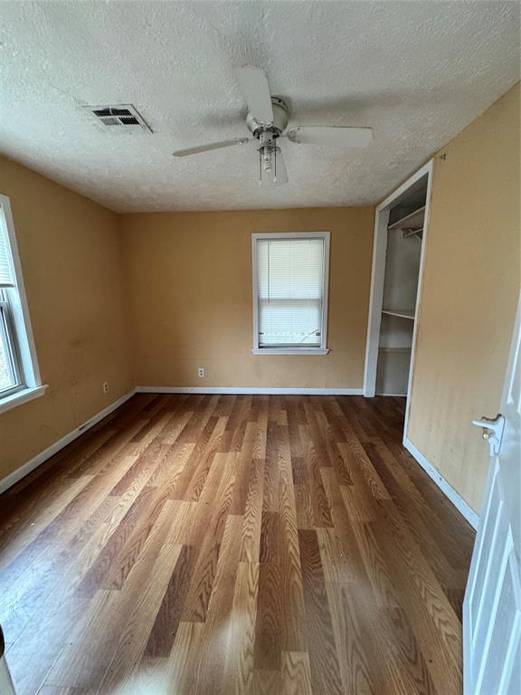 unfurnished bedroom with multiple windows, ceiling fan, a textured ceiling, and hardwood / wood-style flooring