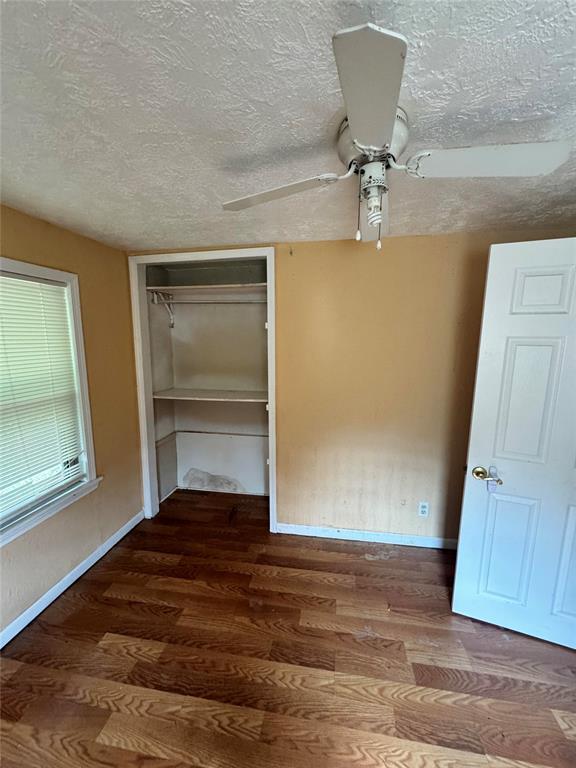 unfurnished bedroom featuring wood-type flooring, a textured ceiling, a closet, and ceiling fan