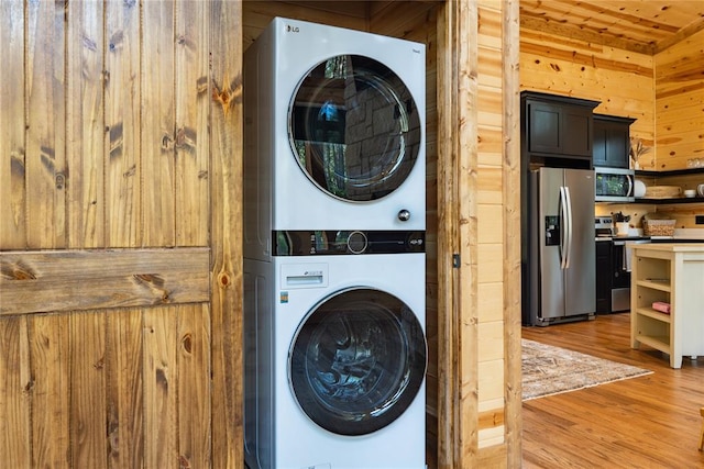 clothes washing area featuring wooden walls, wood-type flooring, stacked washer / drying machine, and wooden ceiling