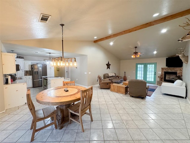 tiled dining area featuring lofted ceiling with beams, ceiling fan with notable chandelier, and a brick fireplace