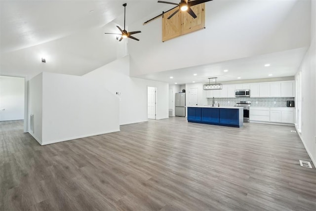 unfurnished living room with ceiling fan, sink, a barn door, high vaulted ceiling, and hardwood / wood-style floors