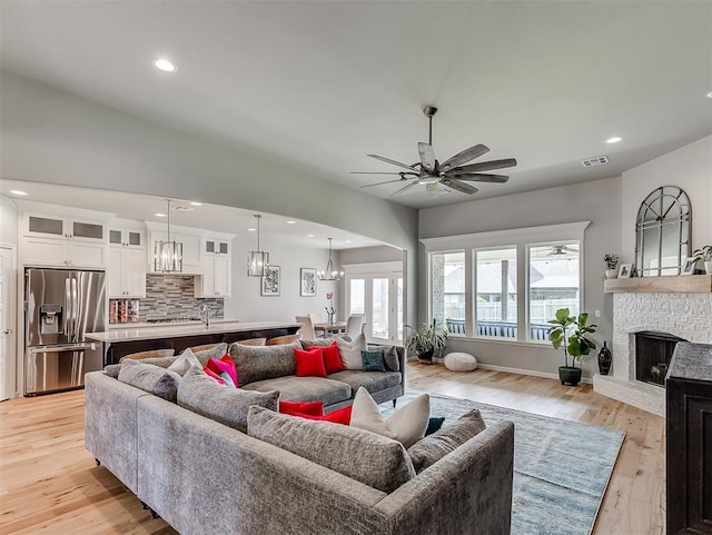 8216 Crew Ln, Edmond, OK 73034 - living room with a chandelier, a ceiling fan, a fireplace with raised hearth, light wood-type flooring, and recessed lighting