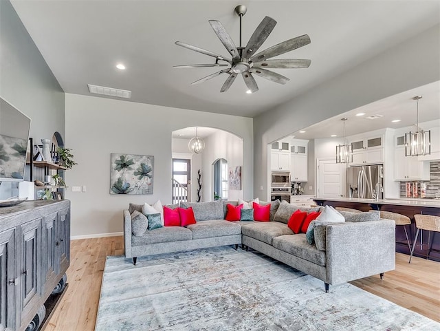 8216 Crew Ln, Edmond, OK 73034 - living room featuring arched walkways, light wood-type flooring, recessed lighting, ceiling fan, and a chandelier