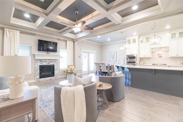 living room with coffered ceiling, ceiling fan, ornamental molding, a fireplace, and light hardwood / wood-style floors