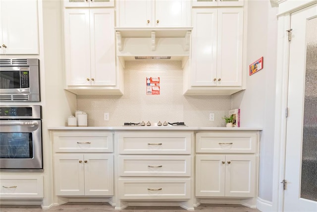 kitchen with backsplash, light hardwood / wood-style flooring, stainless steel appliances, and custom range hood