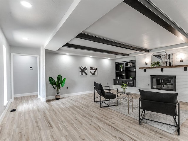 living room with beam ceiling, built in shelves, a fireplace, and light hardwood / wood-style floors