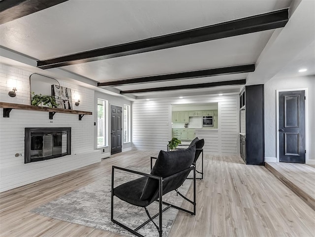 living room featuring beam ceiling, wood walls, light hardwood / wood-style flooring, and a brick fireplace