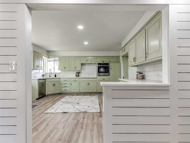 kitchen with sink, stainless steel appliances, green cabinets, backsplash, and light hardwood / wood-style floors