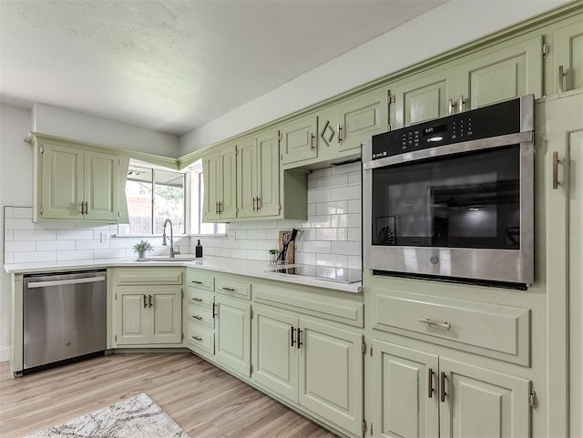 kitchen with sink, tasteful backsplash, light hardwood / wood-style floors, appliances with stainless steel finishes, and green cabinetry