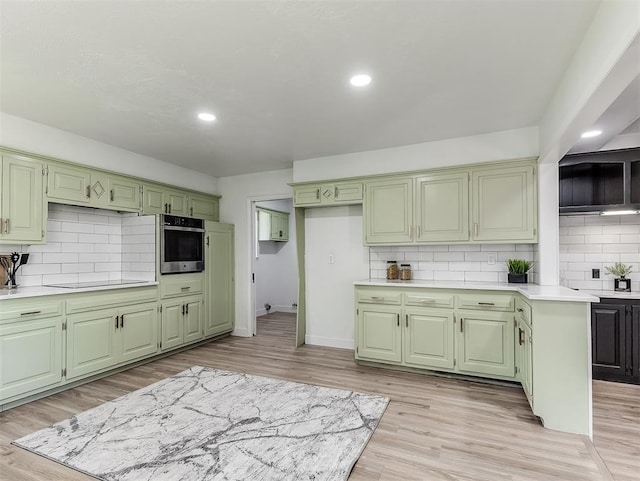 kitchen with oven, tasteful backsplash, light wood-type flooring, and green cabinetry