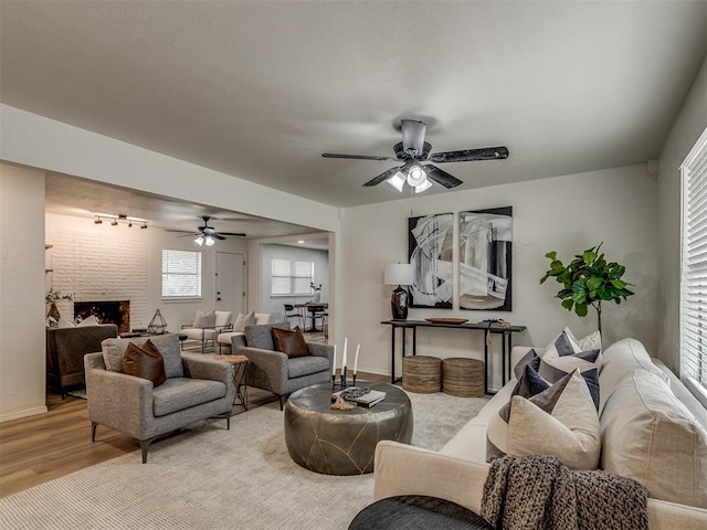 living room featuring a brick fireplace, ceiling fan, rail lighting, and light hardwood / wood-style flooring