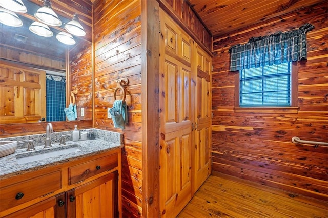 bathroom with hardwood / wood-style flooring, vanity, wood ceiling, and wooden walls