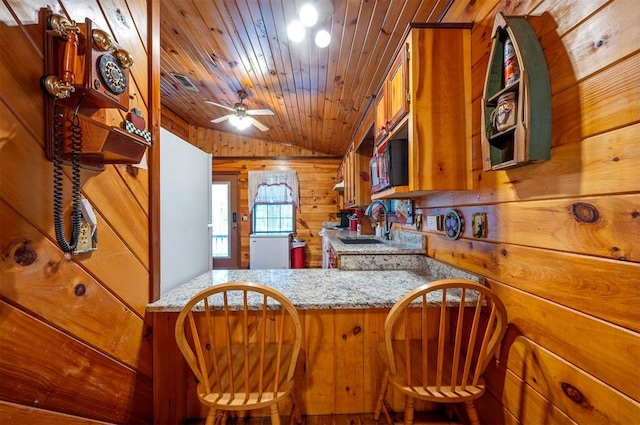 kitchen featuring wood walls, wooden ceiling, ceiling fan, light stone countertops, and kitchen peninsula