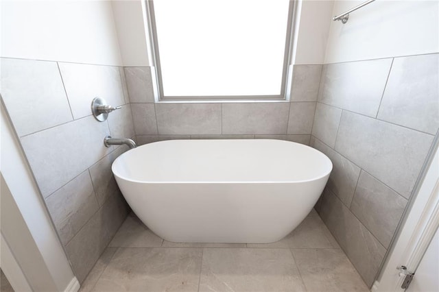 bathroom with tile patterned flooring, a bath, and tile walls