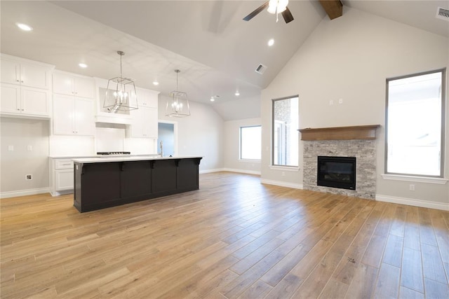 kitchen with light hardwood / wood-style flooring, a stone fireplace, a kitchen island with sink, white cabinets, and decorative light fixtures