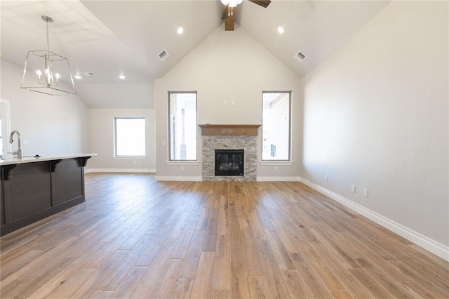 unfurnished living room featuring sink, ceiling fan, high vaulted ceiling, a fireplace, and light hardwood / wood-style floors