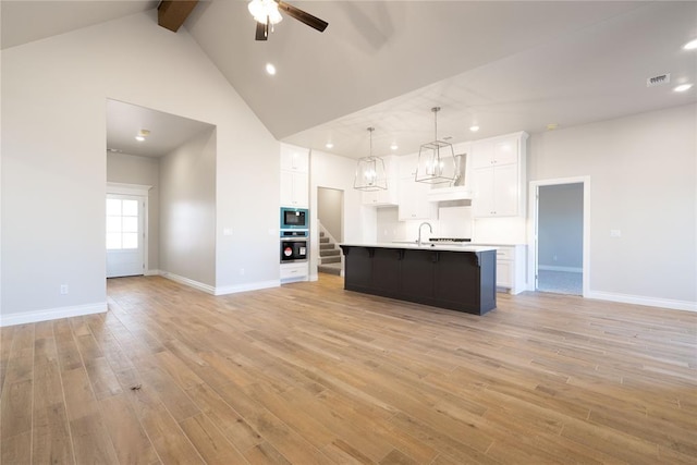 kitchen featuring white cabinetry, a center island with sink, built in microwave, decorative light fixtures, and oven