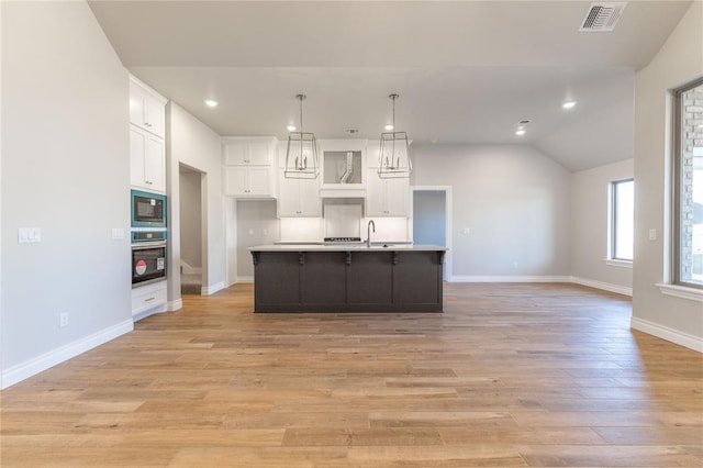 kitchen with pendant lighting, white cabinets, a center island with sink, built in microwave, and oven