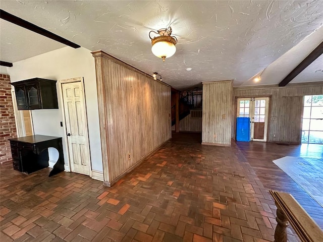 interior space featuring wood walls, beamed ceiling, and a textured ceiling