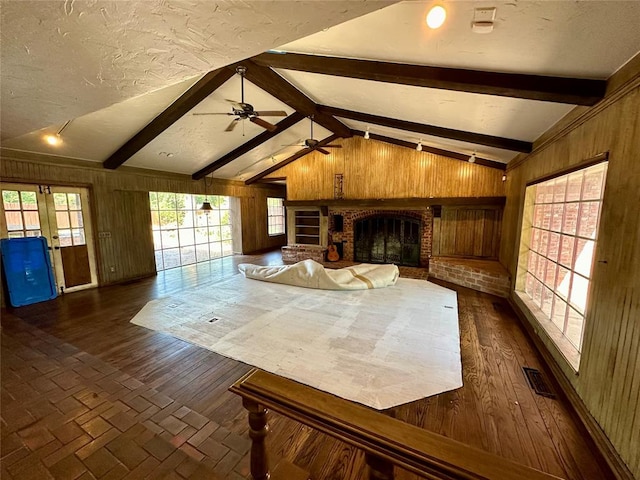 unfurnished living room featuring a fireplace, vaulted ceiling with beams, ceiling fan, and wooden walls