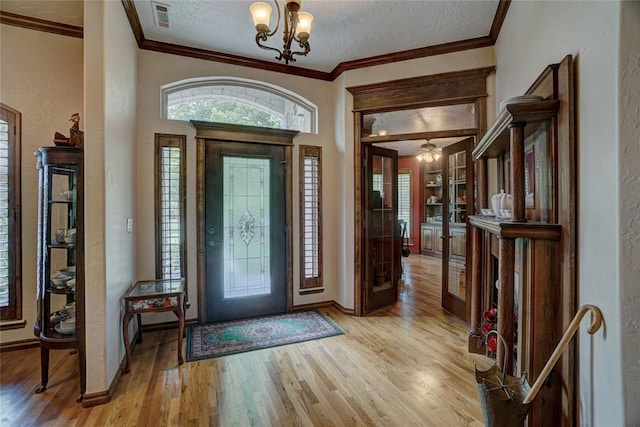 entryway featuring french doors, a notable chandelier, light hardwood / wood-style floors, a textured ceiling, and ornamental molding