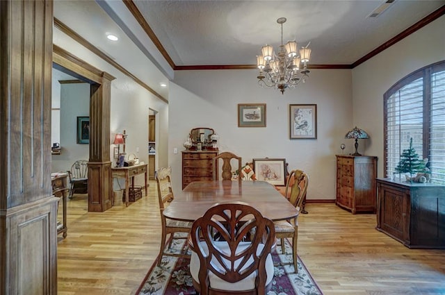 dining room with a notable chandelier, ornate columns, crown molding, and light hardwood / wood-style flooring