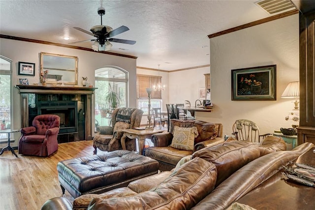 living room featuring hardwood / wood-style floors, a textured ceiling, a fireplace, ceiling fan with notable chandelier, and ornamental molding