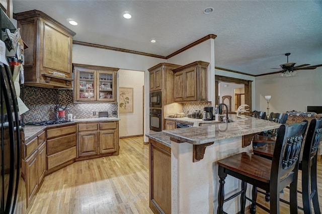 kitchen with ceiling fan, sink, a kitchen bar, black appliances, and light wood-type flooring