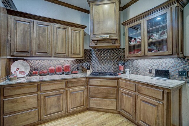 kitchen featuring decorative backsplash, light hardwood / wood-style floors, light stone counters, and ornamental molding