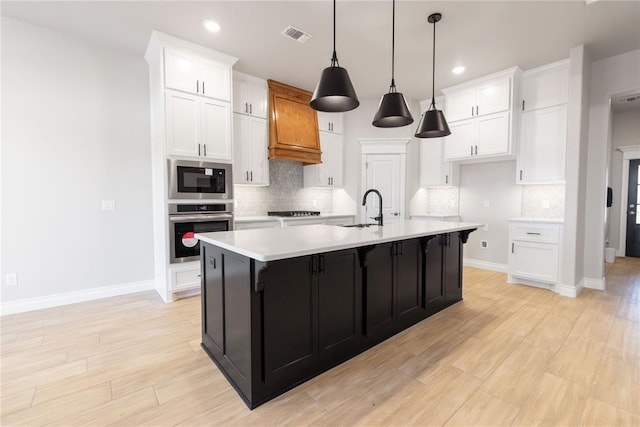 kitchen with stainless steel oven, white cabinets, stovetop, a sink, and premium range hood