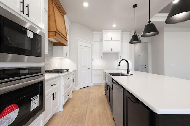 kitchen featuring light countertops, backsplash, appliances with stainless steel finishes, light wood finished floors, and a sink
