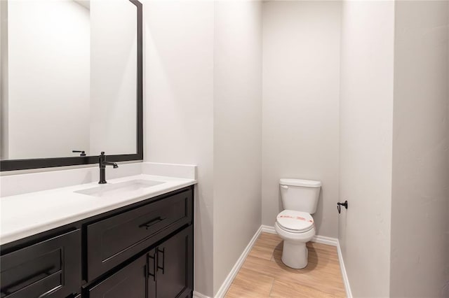 half bath with toilet, wood finished floors, vanity, and baseboards