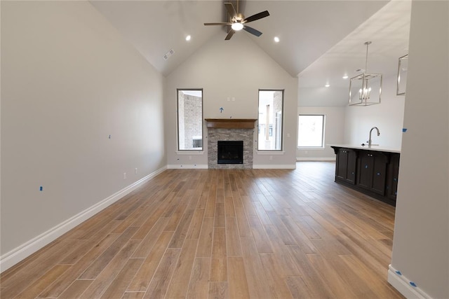 unfurnished living room with a fireplace, light hardwood / wood-style floors, sink, high vaulted ceiling, and ceiling fan with notable chandelier