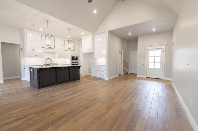 kitchen with light hardwood / wood-style floors, an island with sink, decorative light fixtures, high vaulted ceiling, and white cabinets