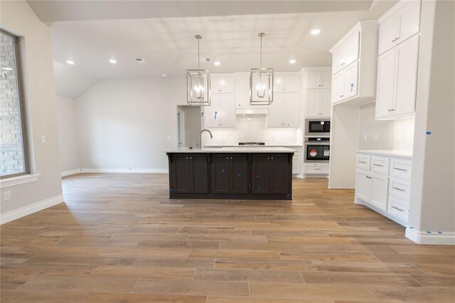 kitchen featuring oven, pendant lighting, white cabinetry, an island with sink, and black microwave