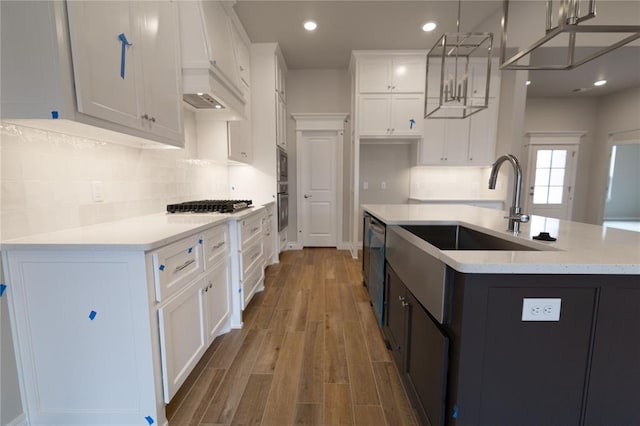 kitchen with pendant lighting, white cabinets, light hardwood / wood-style floors, gas stovetop, and a center island with sink