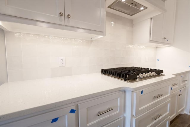 kitchen with stainless steel gas cooktop, white cabinets, tasteful backsplash, and wall chimney range hood