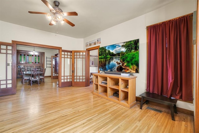 living room featuring ceiling fan with notable chandelier, french doors, and light wood-type flooring