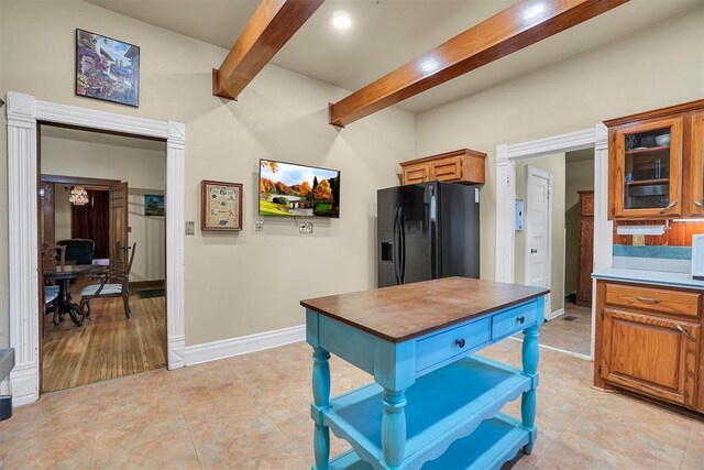 kitchen featuring beamed ceiling, light tile patterned floors, and black refrigerator with ice dispenser