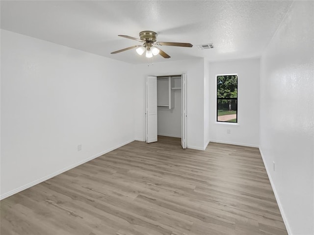 unfurnished bedroom with a textured ceiling, light wood-type flooring, a closet, and ceiling fan