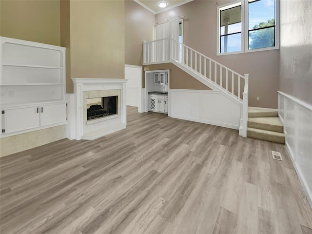 unfurnished living room featuring ornamental molding, a towering ceiling, a fireplace, and light hardwood / wood-style flooring