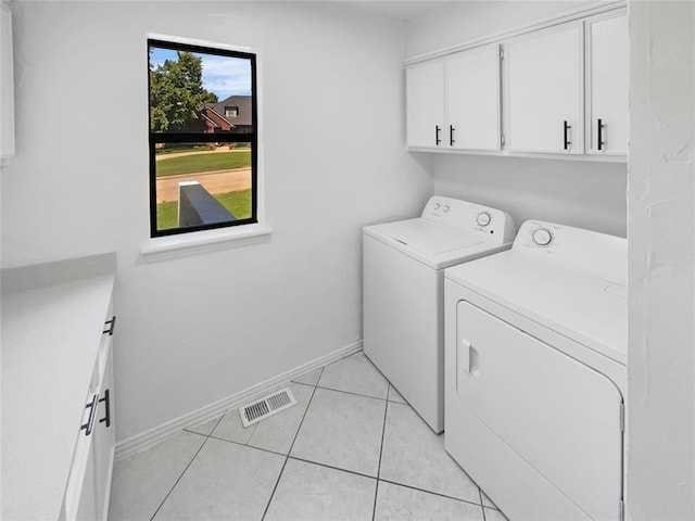 clothes washing area with washer and dryer, light tile patterned flooring, and cabinets