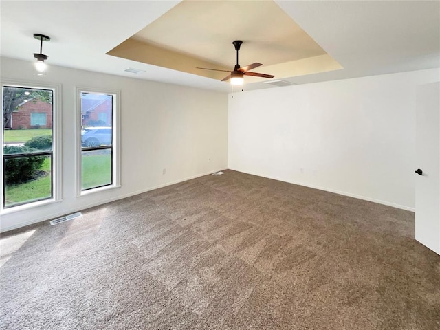 spare room featuring a tray ceiling, ceiling fan, and dark colored carpet