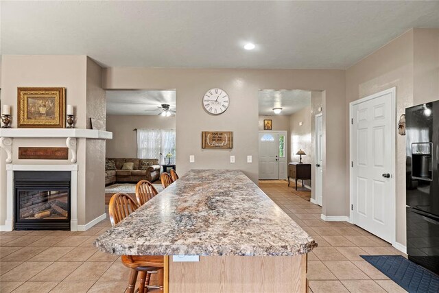 kitchen featuring a kitchen breakfast bar, ceiling fan, black fridge, and light tile patterned floors