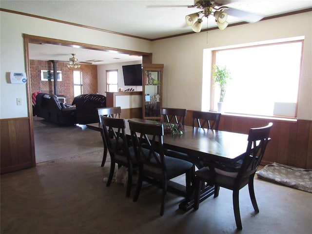 dining area with ceiling fan, a healthy amount of sunlight, and wood walls