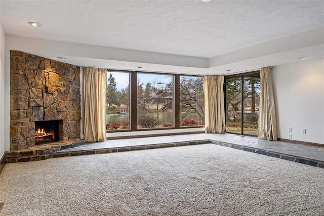 unfurnished living room featuring a stone fireplace, carpet, and a textured ceiling