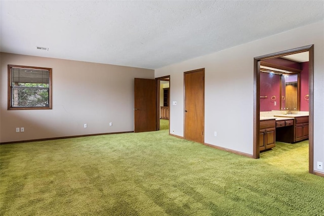 unfurnished bedroom with sink, light colored carpet, a textured ceiling, and ensuite bathroom