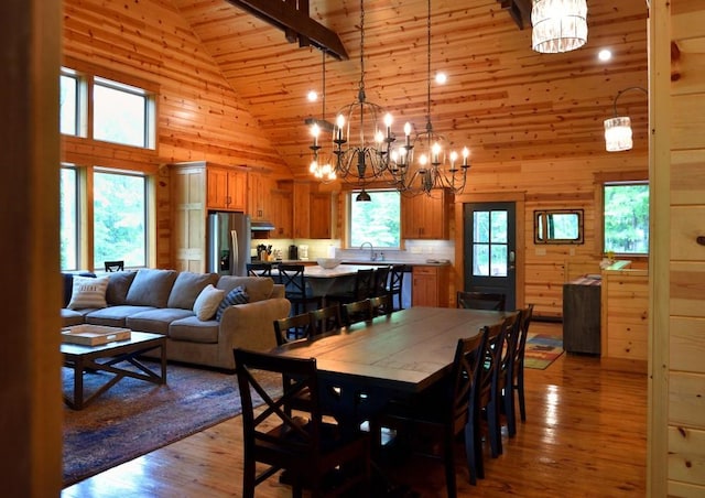 dining space with light wood-type flooring, wooden walls, high vaulted ceiling, and a healthy amount of sunlight