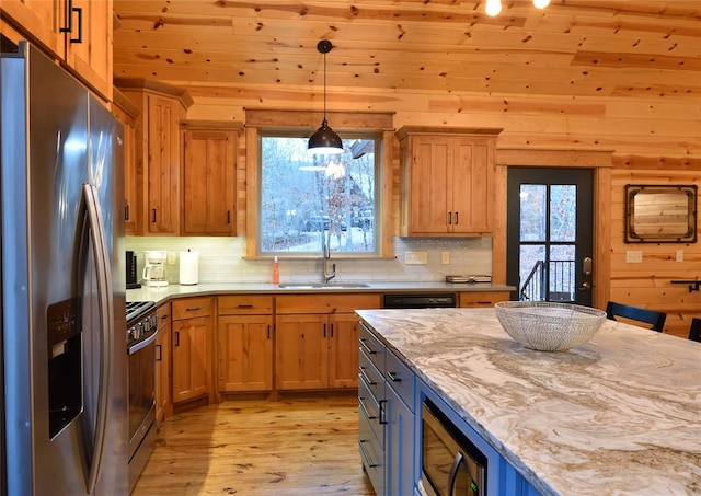 kitchen featuring sink, wooden walls, light wood-type flooring, appliances with stainless steel finishes, and light stone counters