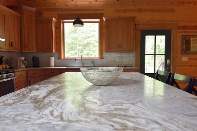 kitchen featuring pendant lighting, wood walls, sink, decorative backsplash, and a breakfast bar area